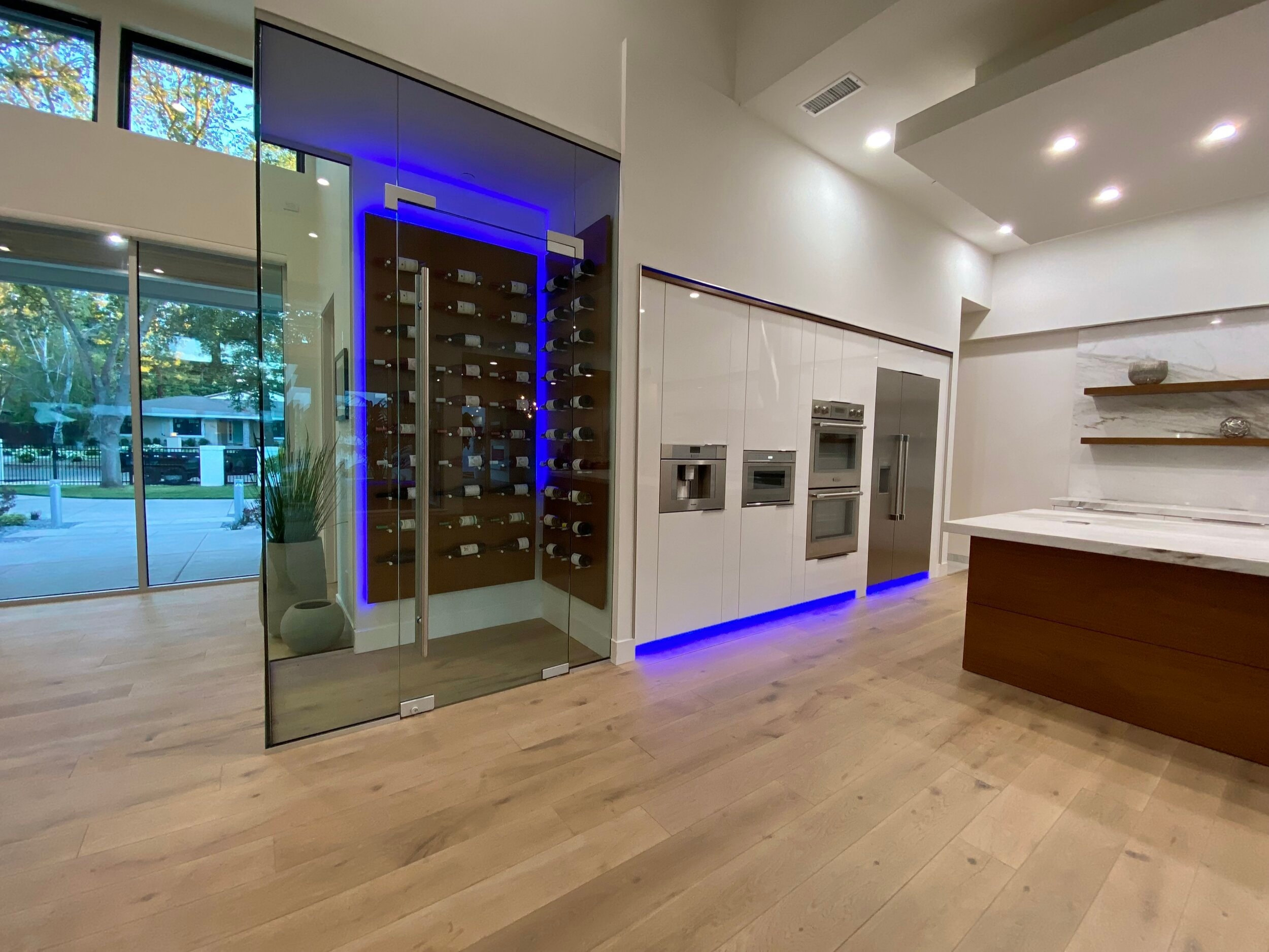 Glass-enclosed wine display with blue accent lighting beside the kitchen