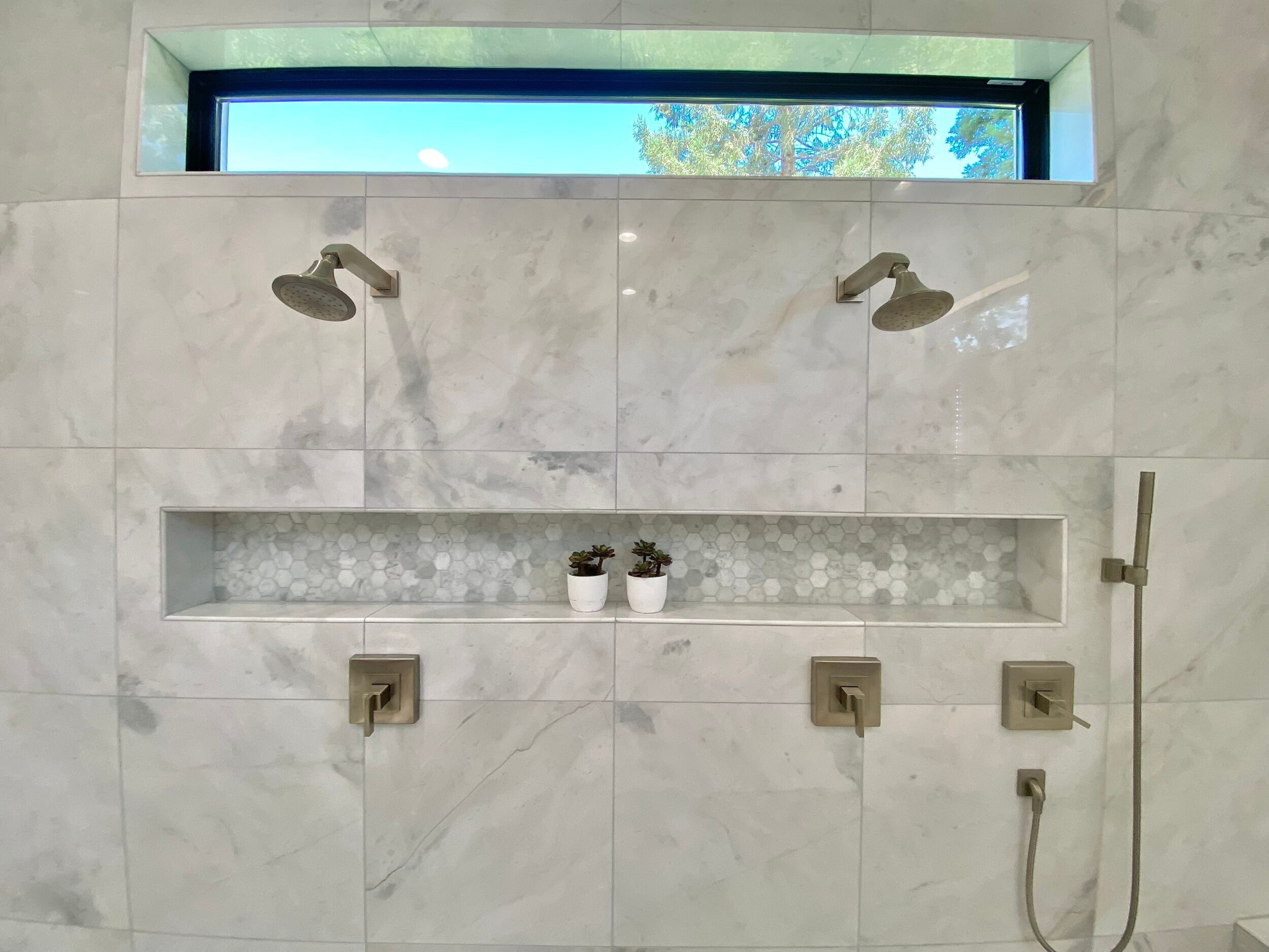 Stone-lined shower with paired showerheads and recessed storage niches