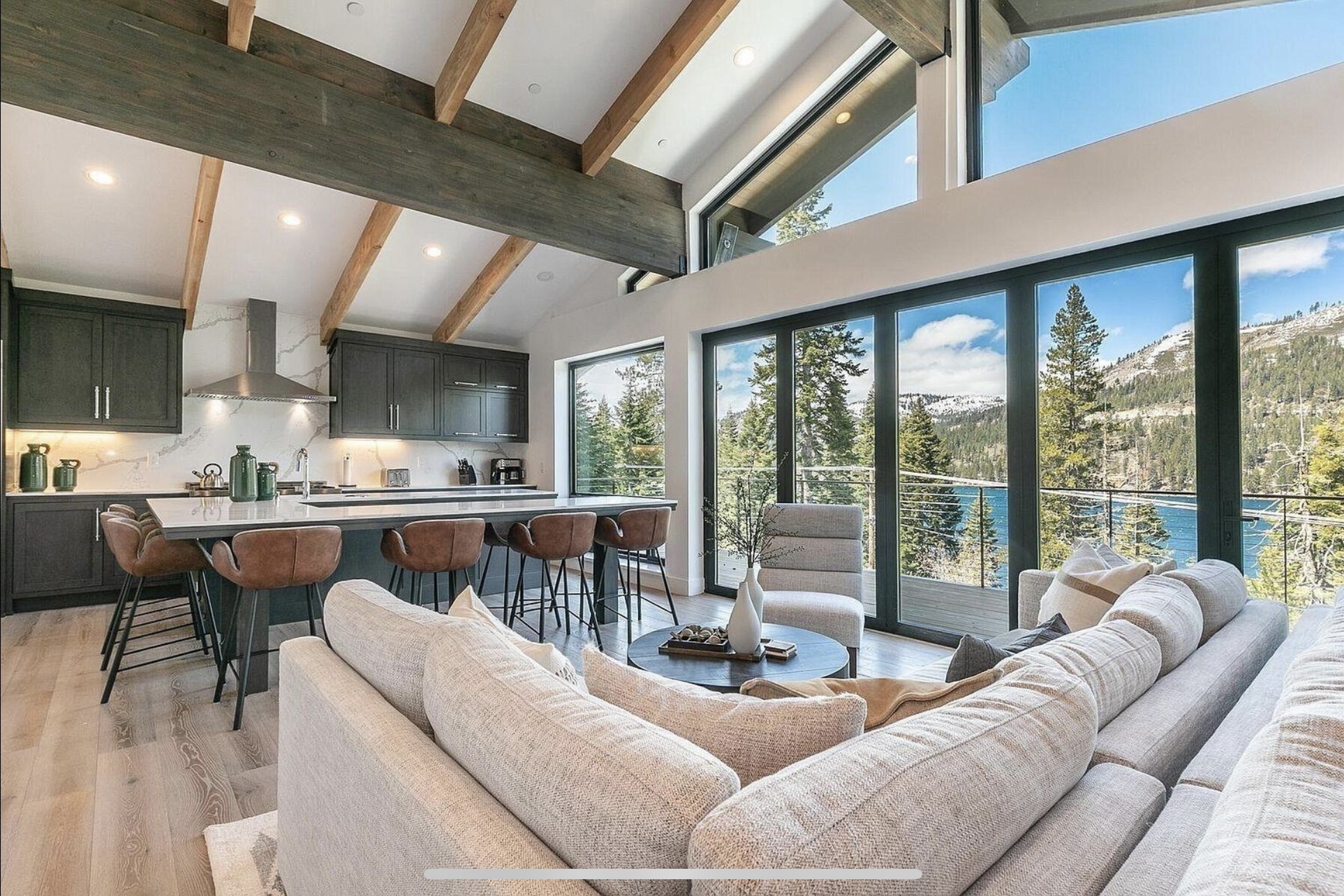 Open great room and kitchen beneath exposed beams, with broad windows facing the lake