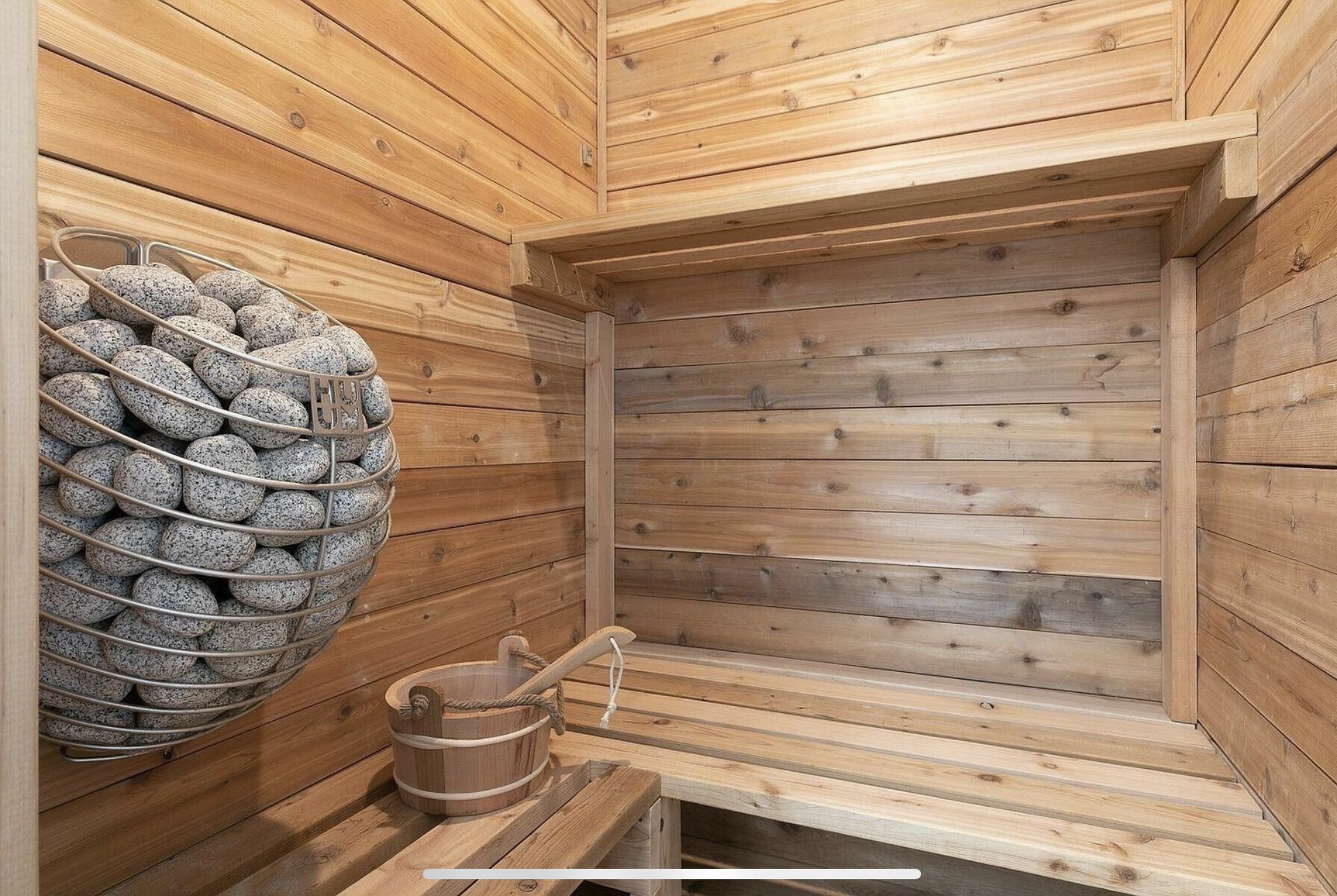 Wood-lined sauna with timber benches and a stone-filled heater