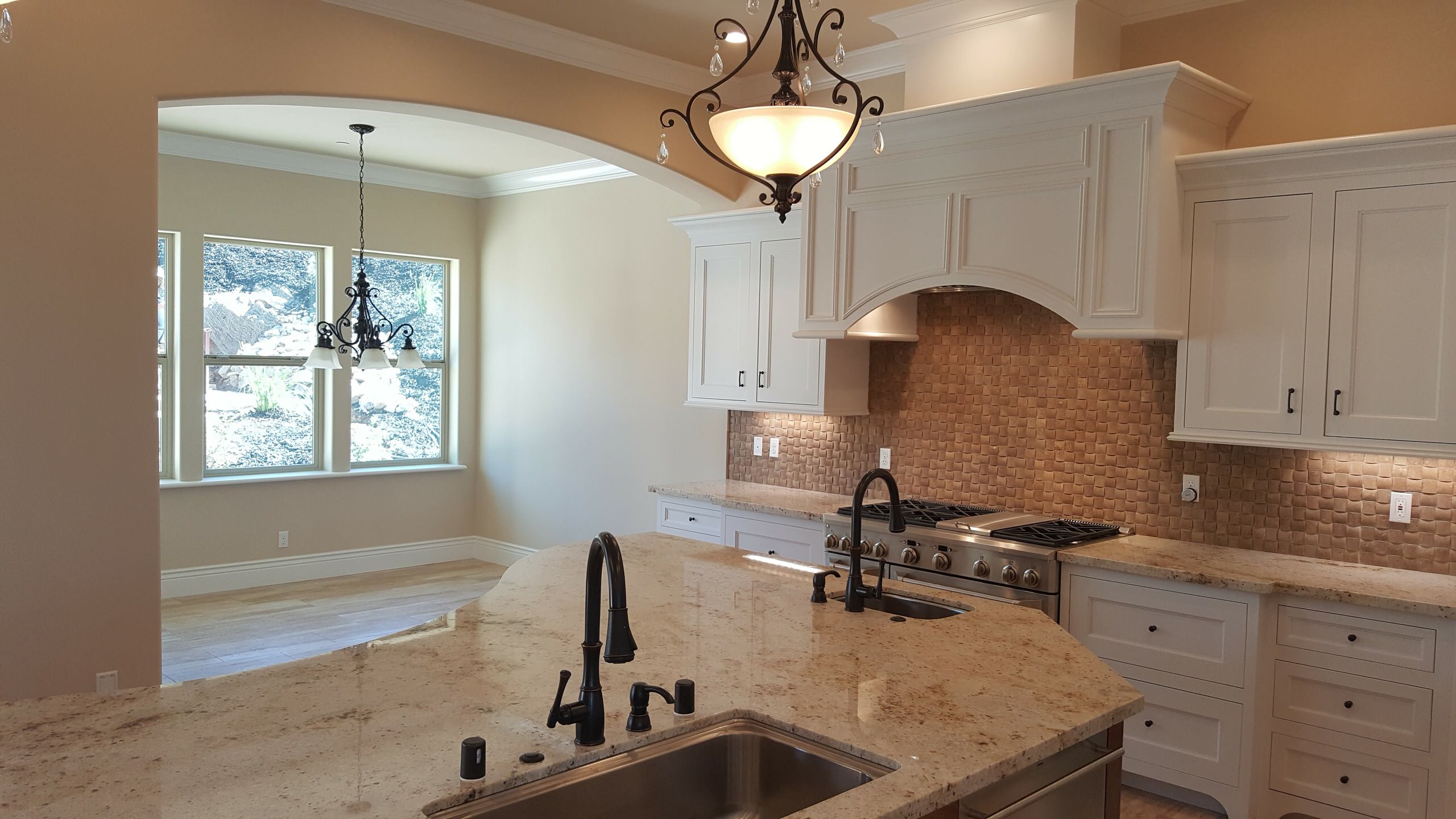 Kitchen sink and cooking area with pale cabinets and a stone backsplash