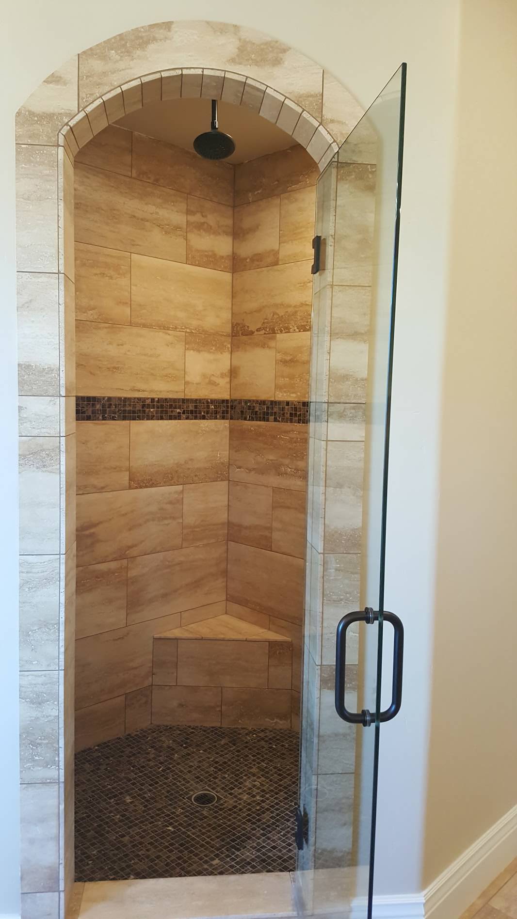 Walk-in shower with warm stone tile and an arched opening